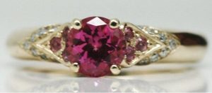 Close up image of a lab-grown round pink sapphire set in a recycled yellow gold engagement ring accented by small natural pink sapphires and white diamonds